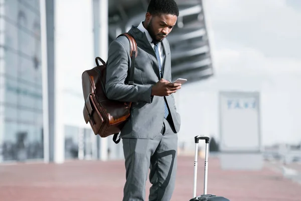 Podnikatel pomocí Smartphone Travel App stojící se zavazadly na letišti — Stock fotografie