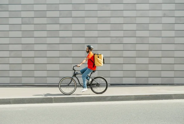Un repartidor en bicicleta. Joven con barba y gran mochila pasea por el camino de la ciudad — Foto de Stock