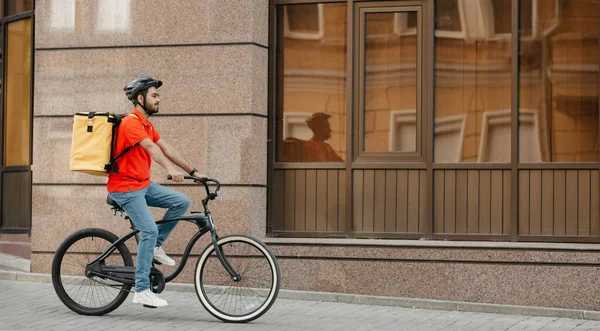 Entrega, trabalho e desporto. Jovem com barba no capacete com mochila anda de bicicleta na rua — Fotografia de Stock