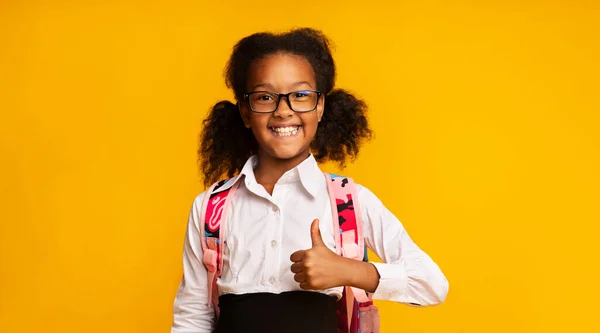 Veselý černošky školní dívka gesturing palce nahoru pózování přes žluté pozadí — Stock fotografie
