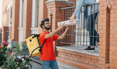 Kurye ve müşteriyle buluşacağım. Kasklı, büyük sarı sırt çantalı, bisikletli gülümseyen teslimatçı müşteri için pizza getirdi.