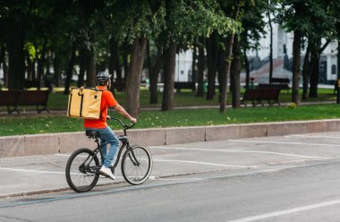 Kurye bisiklet teslimat servisi. Parktaki yolda büyük sarı sırt çantalı bir adam.