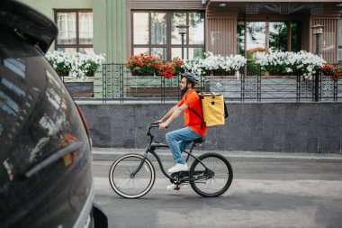 Şehirde iş günü kuryesi. Sırt çantalı, yolda bisiklet süren kasklı genç bir adam.