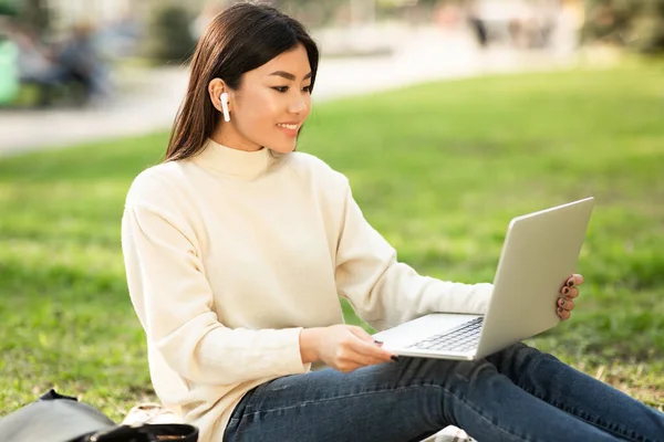 Azji młoda kobieta za pomocą laptopa, siedzi w parku — Zdjęcie stockowe
