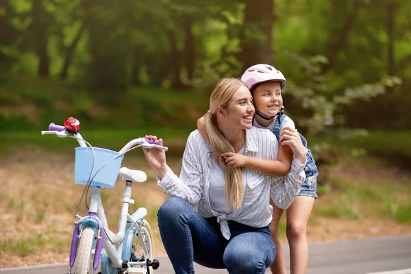 娘は公園で自転車に乗ることを学ぶ母親を抱きます — ストック写真