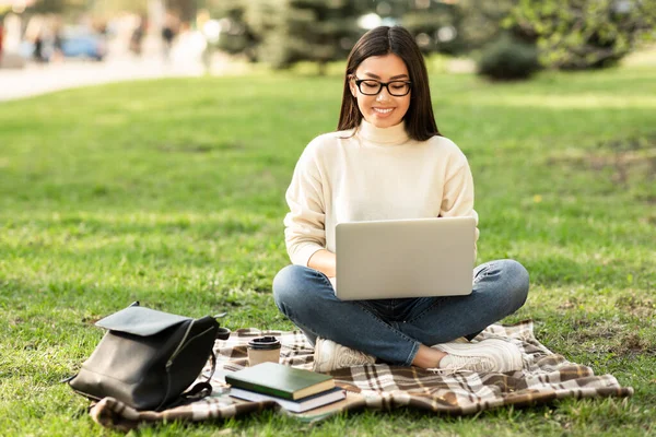 Estudiante en especificaciones usando laptop, sentado en el parque — Foto de Stock