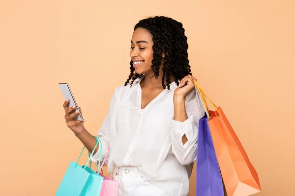 Felice ragazza nera utilizzando Smartphone Holding Shopper Borse, Studio Shot — Foto Stock