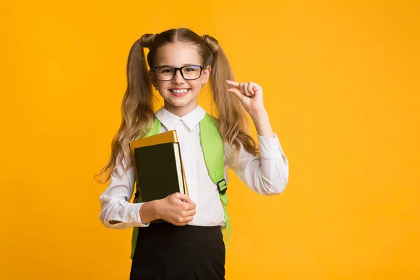 Nerdy školní dívka drží knihy gesta potřebují více, žluté pozadí — Stock fotografie