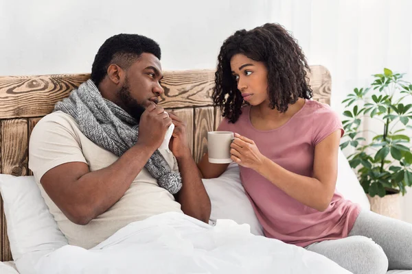Uppmärksam svart fru ger sin sjuke man varm dryck — Stockfoto