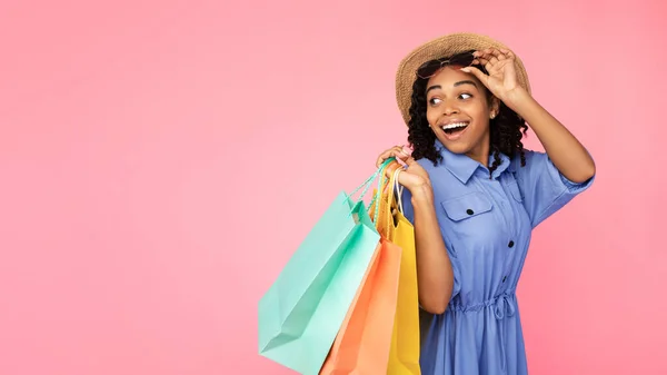 Emocionada chica africana llevando bolsas de compras mirando a un lado, fondo rosa —  Fotos de Stock