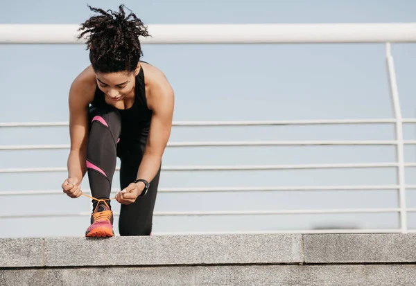 Início do treino matinal. jovem afro-americano em sportswear com rastreador de fitness amarrando cadarços no estádio — Fotografia de Stock