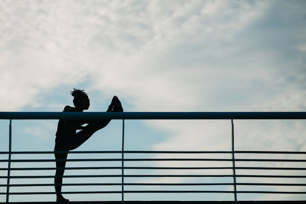 Stretching outdoors. Silhouette of african american woman, doing exercise at stadium