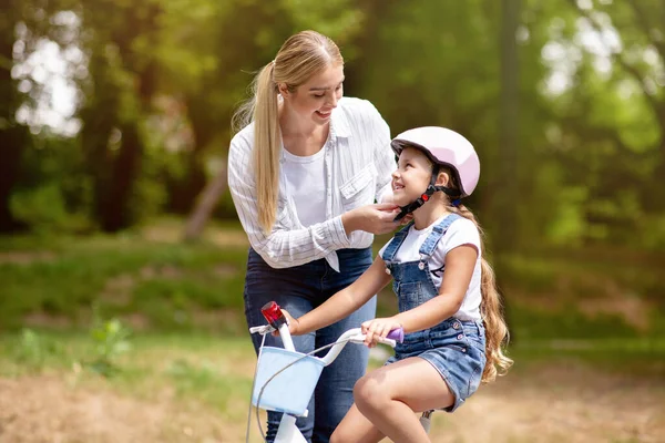 Mor undervisning dotter till cykel, sätta hjälm på Kid utomhus — Stockfoto