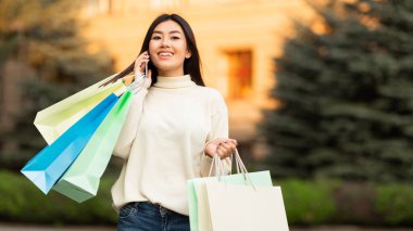 Asyalı kız şehir merkezinde telefonla konuşuyor.