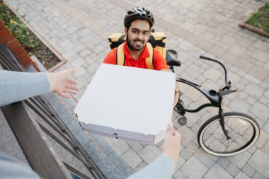 İnternetten sipariş ve evde pizza. Kasklı gülümseyen kurye, evin yakınındaki müşteriye kutular veriyor.