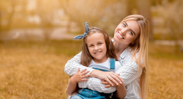 Young Mother Hugging Little Daughter Sitting In Park In Autumn