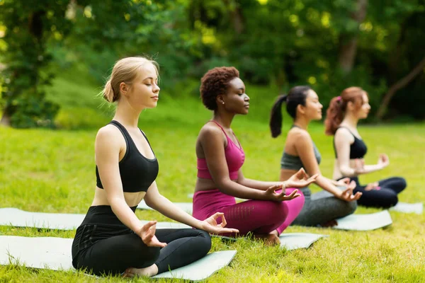 Mujeres multinacionales concentradas en meditación durante la clase de yoga al aire libre en el parque, espacio vacío — Foto de Stock