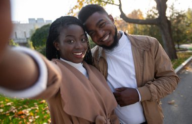 Neşeli Afrikalı Amerikalı çift parkta yürürken kendi portrelerini çekiyorlar.