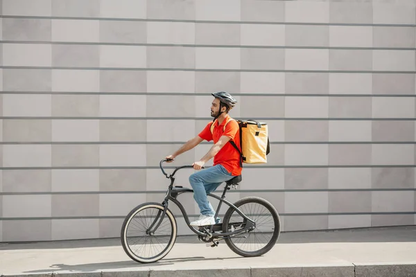 Joven ciclista hombre caucásico en casco protector con mochila a caballo bicicleta en la acera con mochila en la ciudad — Foto de Stock