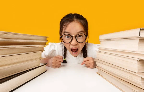 Wütendes chinesisches Schulmädchen schreit vor Büchern über gelbem Hintergrund — Stockfoto