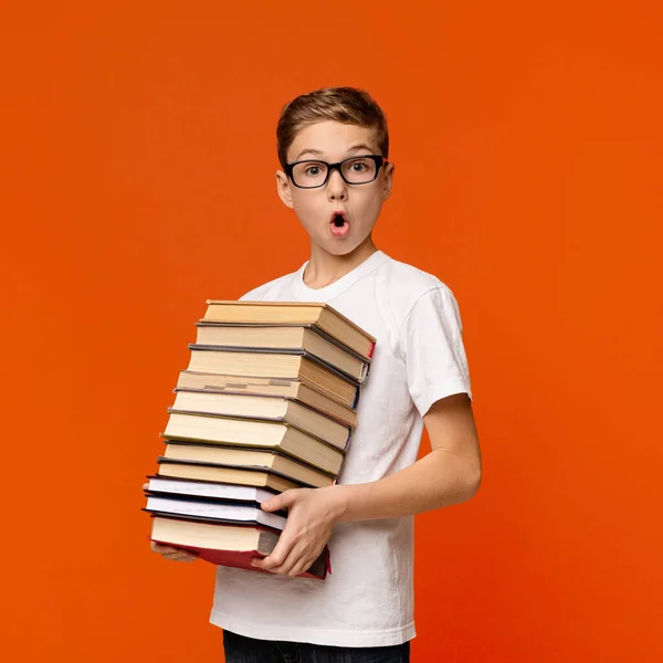Zszokowany uczeń w okularach trzymający stos książek — Zdjęcie stockowe