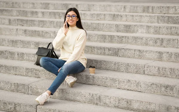 Студентка за допомогою телефону, сидить на сходах — стокове фото