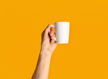 Turuncu arka planda elinde bir bardak sıcak içecek tutan genç adam, elini kapat.