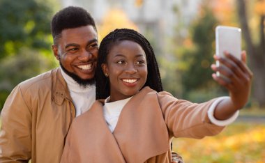 Romantik Afrikalı Amerikalı çift dışarıda akıllı telefonlarıyla selfie çekiyor.