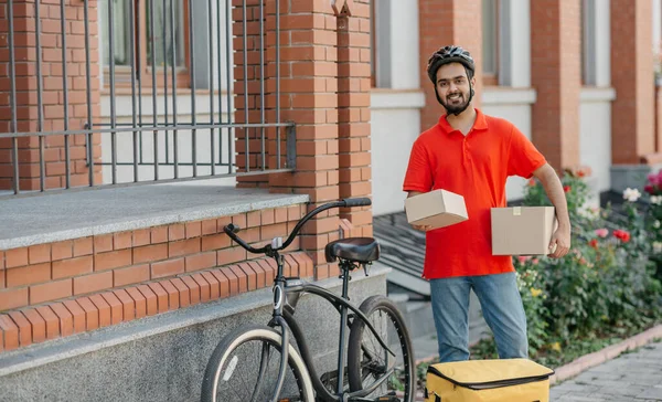 Çevrimiçi alımlar için hızlı teslimat. Sakallı gülümseyen kurye karton kutular tutuyor.