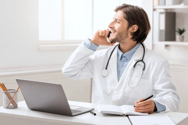 Joven médico hablando con el paciente a través del teléfono celular en el consultorio — Foto de Stock