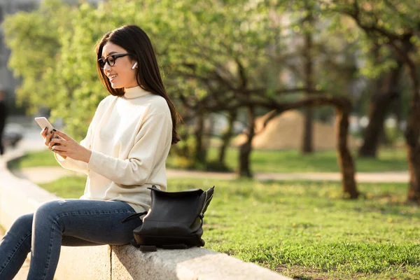 Telefon kullanan, parkta oturan bir kız öğrenci. — Stok fotoğraf