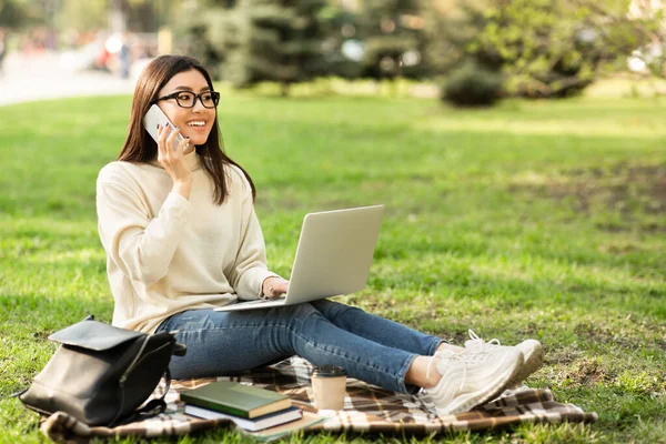 Telefon ve dizüstü bilgisayar kullanan kız öğrenci, parkta oturuyor.