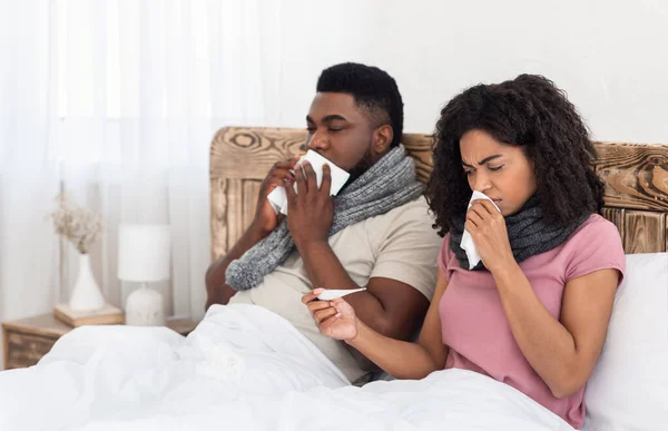 Pasangan hitam sakit duduk di tempat tidur, mengukur demam, bersin hidung — Stok Foto