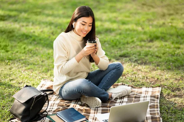 Öğrenci kahve içiyor, laptop kullanıyor, parkta oturuyor. — Stok fotoğraf