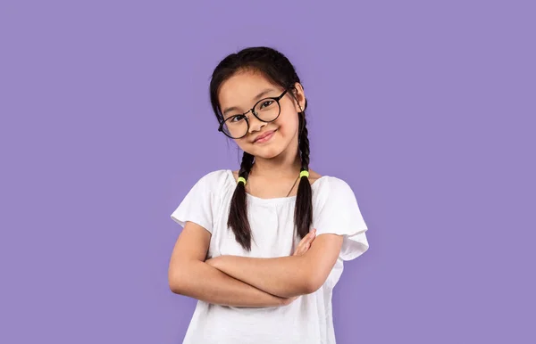 Pequeña chica china con anteojos posando cruzando las manos, fondo púrpura — Foto de Stock