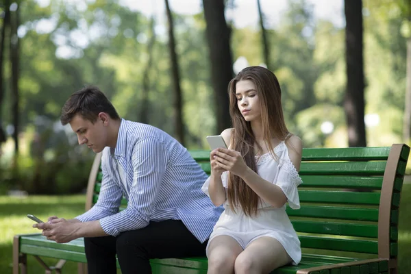 Vício em gadgets. Casal jovem com telefones celulares negligenciando uns aos outros no parque — Fotografia de Stock