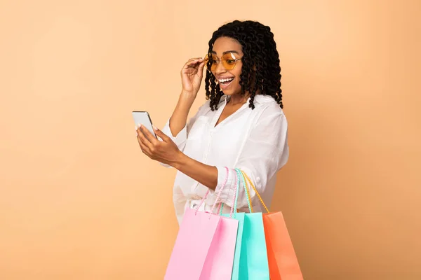 Africano ragazza utilizzando telefono posa con shopping borse in studio — Foto Stock