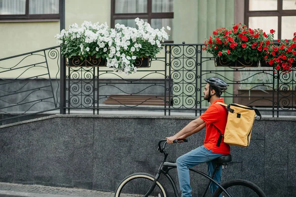 Kurýr provádí objednávky na dodání zboží. Muž v helmě a velký žlutý batoh jezdí na kole — Stock fotografie