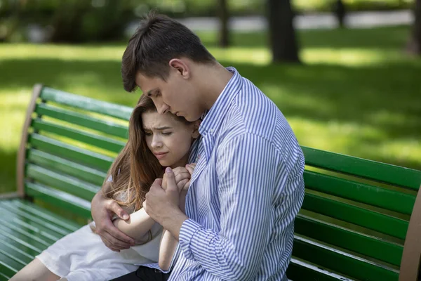 Joven consolando a su novia molesta en el banco en el parque — Foto de Stock