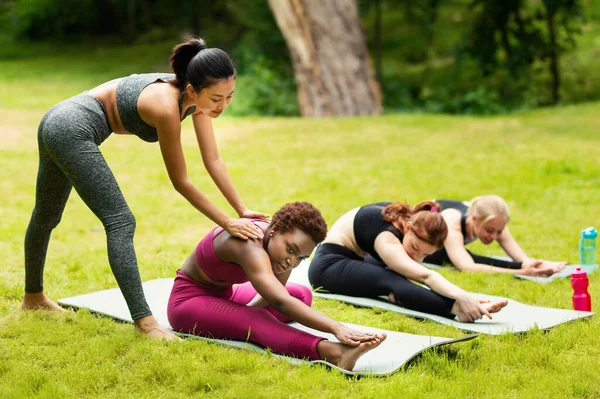 Professor de ioga assistindo jovem mulher durante a aula de grupo ao ar livre no parque — Fotografia de Stock