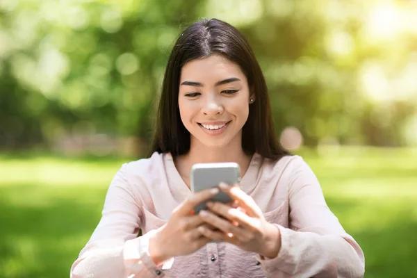 Joyeuse asiatique fille messagerie sur Smartphone en plein air, bavarder avec des amis — Photo