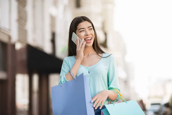Neşeli Asyalı kız cep telefonuyla konuşuyor ve dışarıda alışveriş torbalarıyla yürüyor.. — Stok fotoğraf
