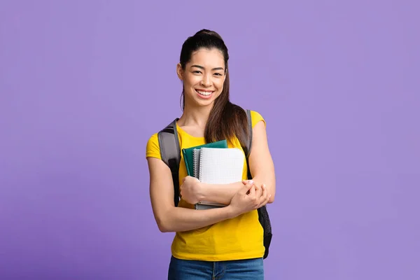 Portret van aziatische student meisje met rugzak en werkboeken over paarse achtergrond — Stockfoto