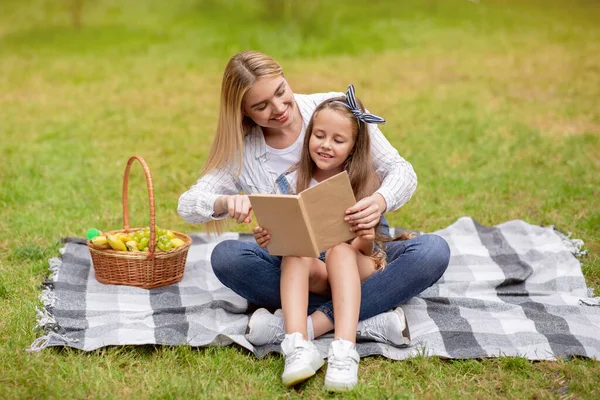 Kislány és az anyja olvasó könyv piknik kívül — Stock Fotó