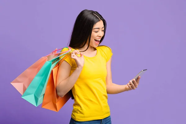Cashback. felice asiatico ragazza con shopping borse guardando Smartphone con eccitazione — Foto Stock