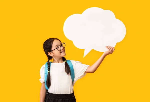 Asiático estudante segurando branco discurso bolha posando sobre fundo amarelo — Fotografia de Stock