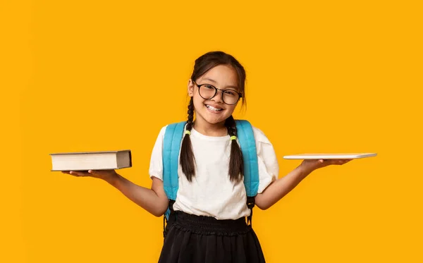 Menina da escola asiática comparando Digital Tablet e livro, fundo amarelo — Fotografia de Stock