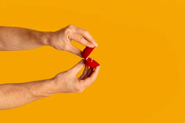 Крупним планом тисячолітній хлопець відкриває коробку з кільцем заручин на помаранчевому фоні, копіювати простір — стокове фото
