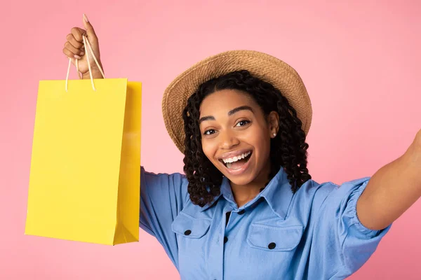 Чернокожая женщина делает селфи в магазине, держа сумку на розовом фоне — стоковое фото