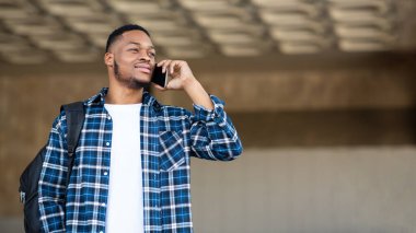 Siyahi adam şehirde dikilip telefonla konuşuyor.
